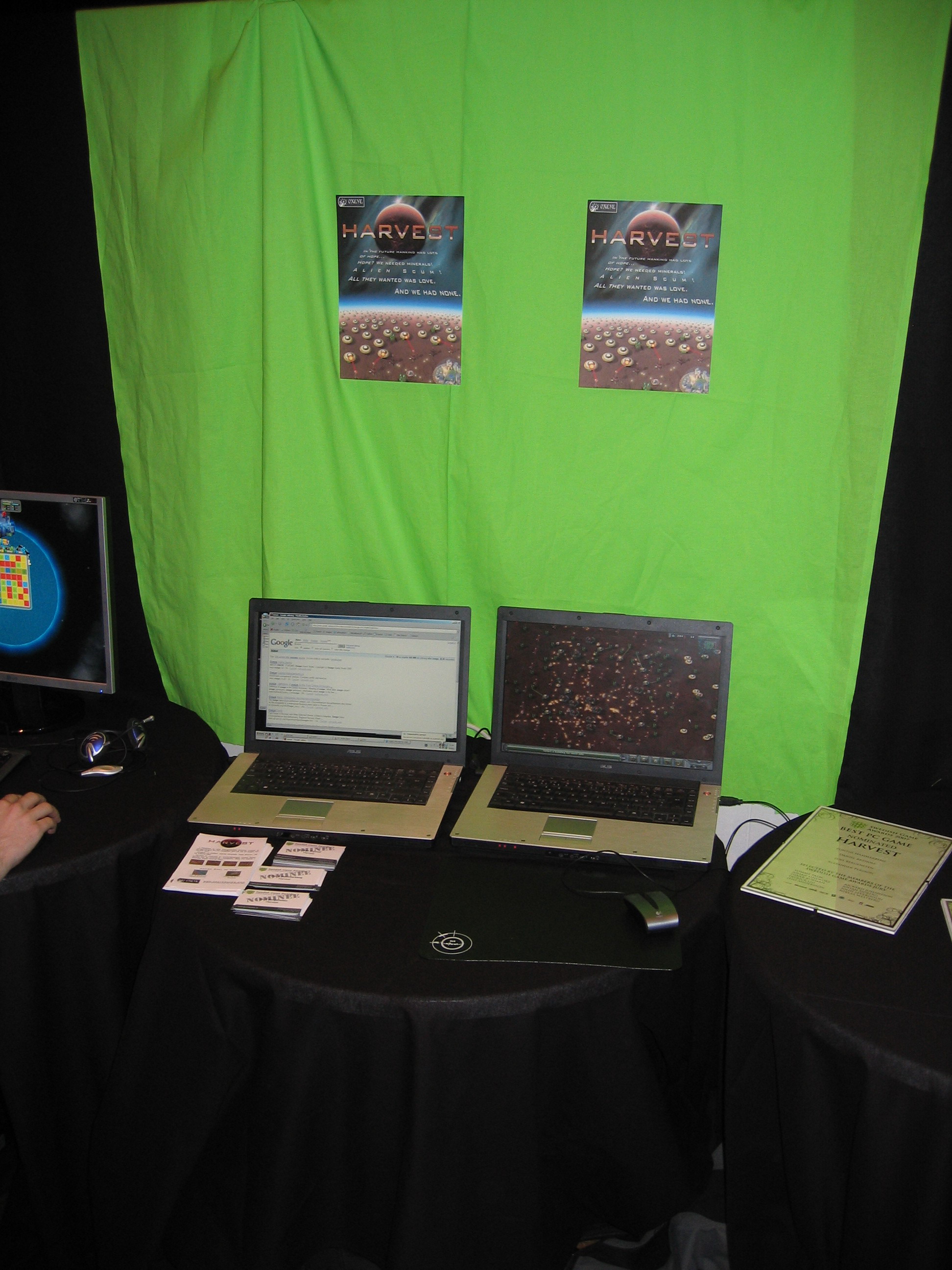 A picture of the Harvest: Massive Encounter stand at the Swedish Game Awards, featuring two laptops with the game in front of a green canvas with posters of the game.