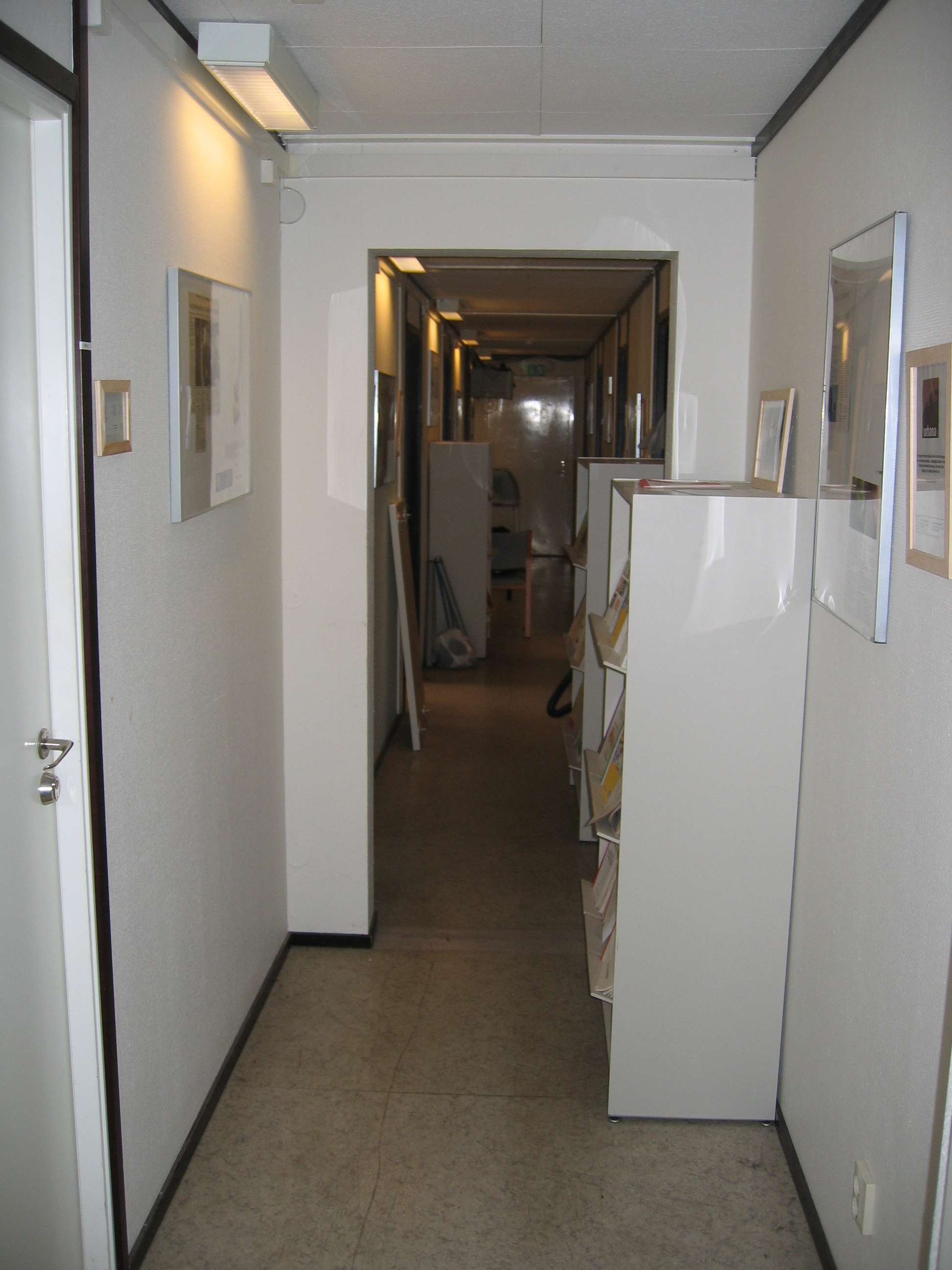 A picture of a narrow, interior corridor of the VentureLab office, including some shelves and framed images on the wall.
